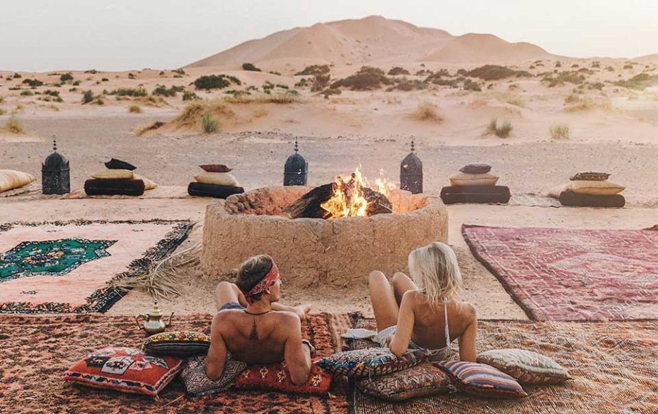 Two influencers looking the Sahara desert of Merzouga in Morocco around the firepit in a camp.
