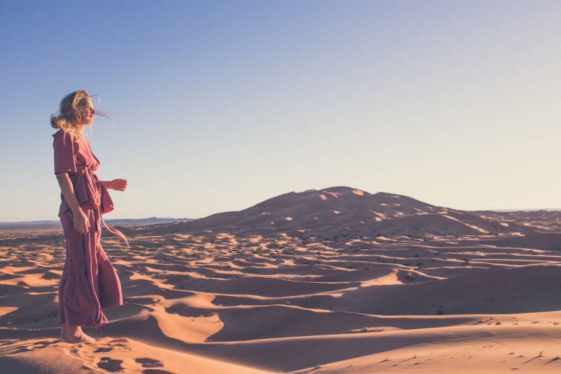 A girl in the desert looking at the sun, in her thoughts.